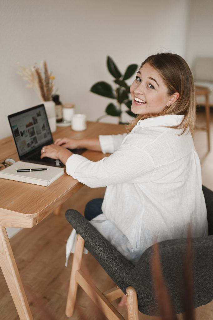 Das Bild zeigt die Coachin am Schreibtisch lachend arbeiten.