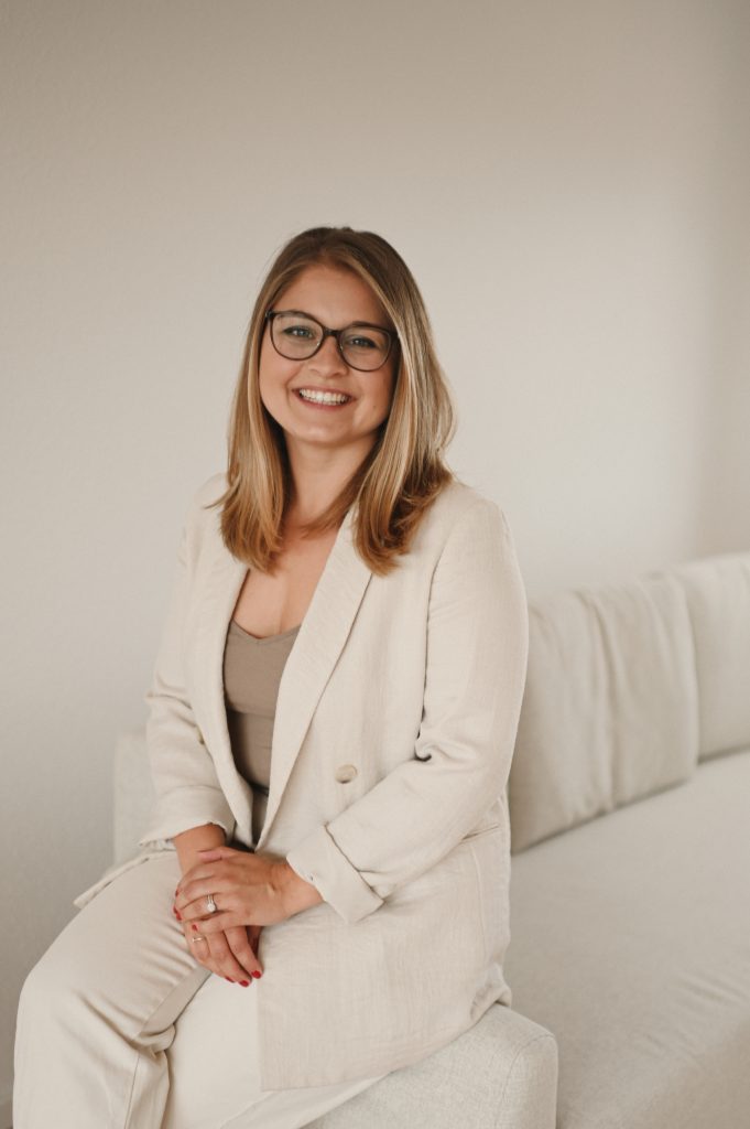 Das Bild zeigt die lachende Coachin auf der Sofalehne sitzend.